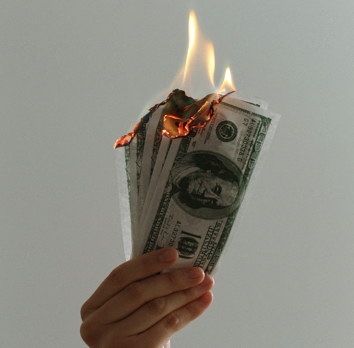 a hand holding money with flames coming off the top